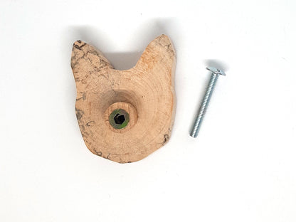 Paire de poignées en bois massif en forme de tête de chat, sculptées à partir de rondins de bois naturel avec leurs cernes visibles. Sur des portes blanches, elles apportent une touche artisanale et originale au mobilier. Fabrication artisanale