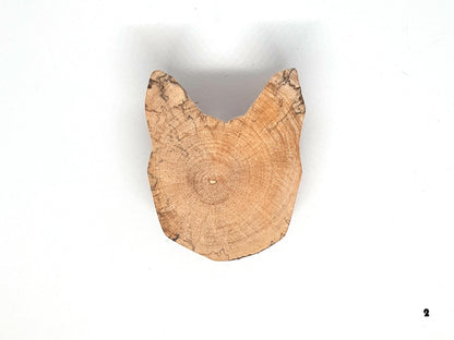 Paire de poignées en bois massif en forme de tête de chat, sculptées à partir de rondins de bois naturel avec leurs cernes visibles. Sur des portes blanches, elles apportent une touche artisanale et originale au mobilier. Fabrication artisanale