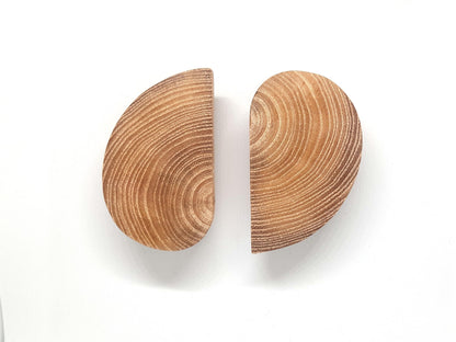 Poignées de meuble en bois en forme de demi-cercle fixées sur deux portes blanches adjacentes. L’effet visuel crée un cercle complet lorsqu’elles sont fermées. Design minimaliste et naturel, idéal pour une décoration intérieure scandinave ou moderne. Le bois brut met en valeur les veines naturelles pour un rendu chaleureux. Image parfaite pour illustrer des idées de poignées originales ou de meubles sur mesure.