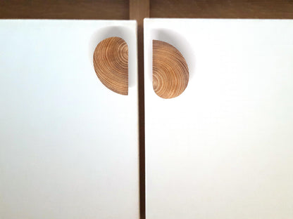 Détail de poignées de meuble en bois de forme semi-circulaire fixées sur deux panneaux blancs. L’alignement parfait de ces poignées crée un effet visuel circulaire esthétique, soulignant un style épuré et nordique. Cette solution de design unique est idéale pour des cuisines, dressings ou rangements modernes. Un exemple inspirant pour l’aménagement intérieur et la décoration avec des matériaux naturels.